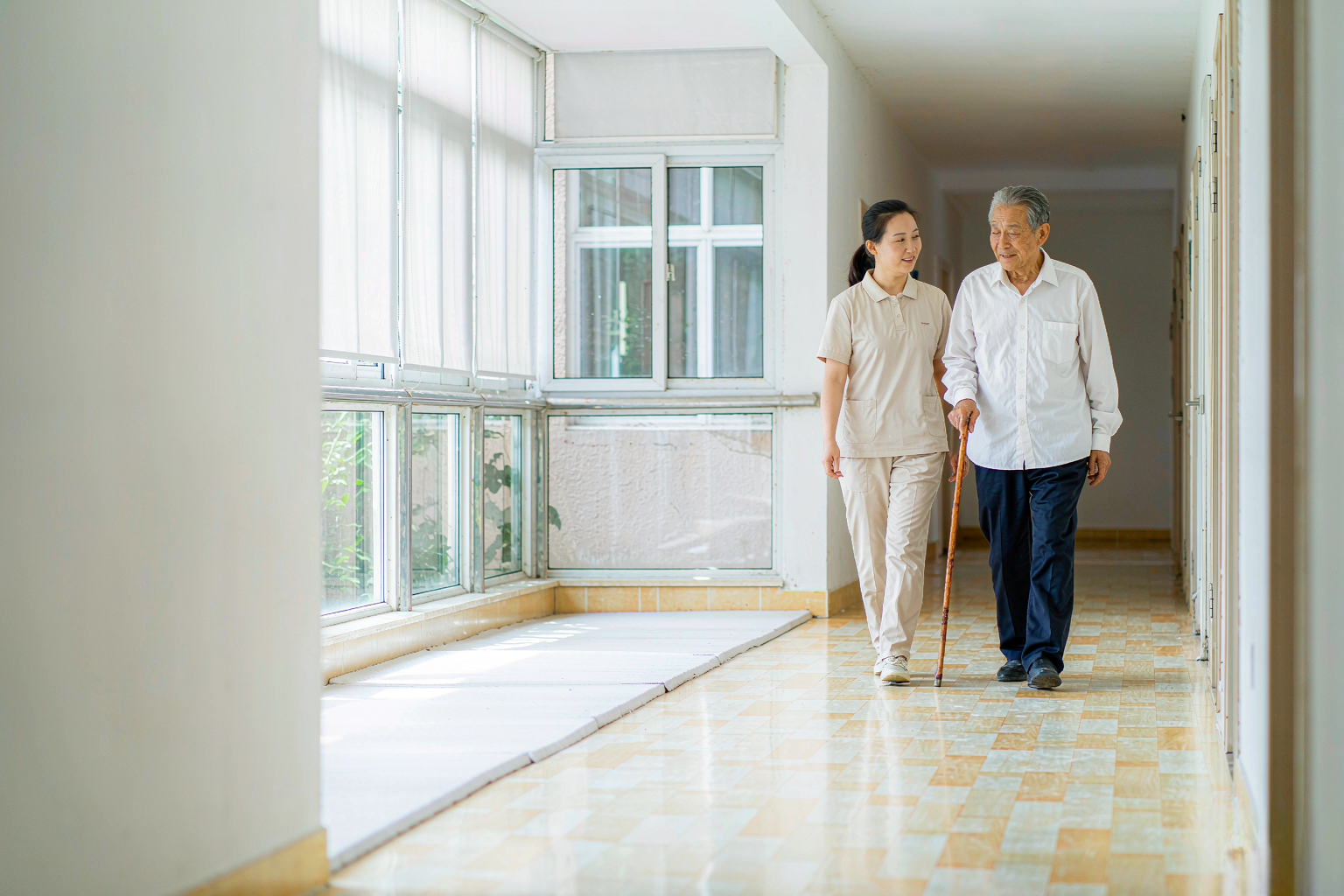 上海养老院明亮走廊,护理员在旁照看慢行的老人,自然光洒进室内 上海养老院明亮走廊,护理员在旁照看慢行的老人,自然光洒进室内
