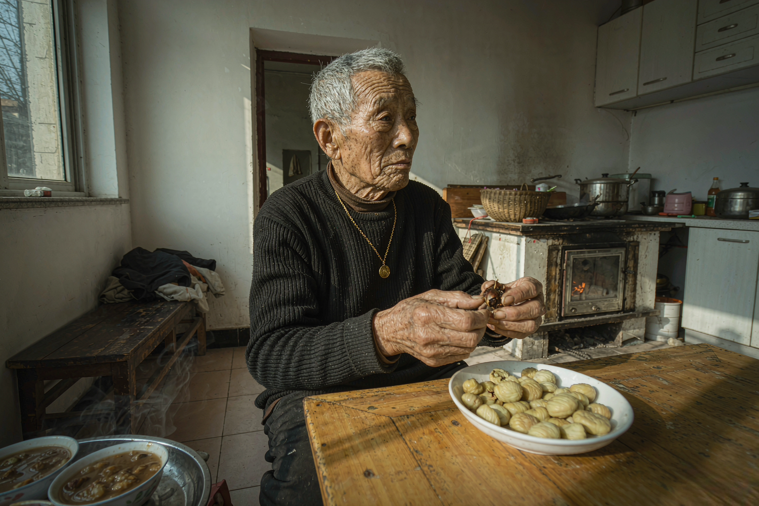 老人冬天吃板栗要控制数量 冬日厨房里中国老人坐在餐桌前剥热板栗桌上一碗蒸板栗