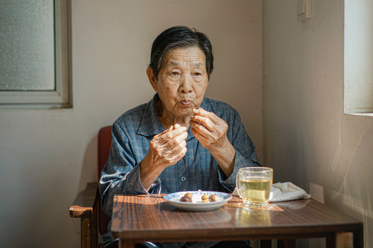 老人吃板栗细嚼慢咽适量饮水 中国老人在客厅茶几旁细嚼慢咽吃板栗旁边一杯温水
